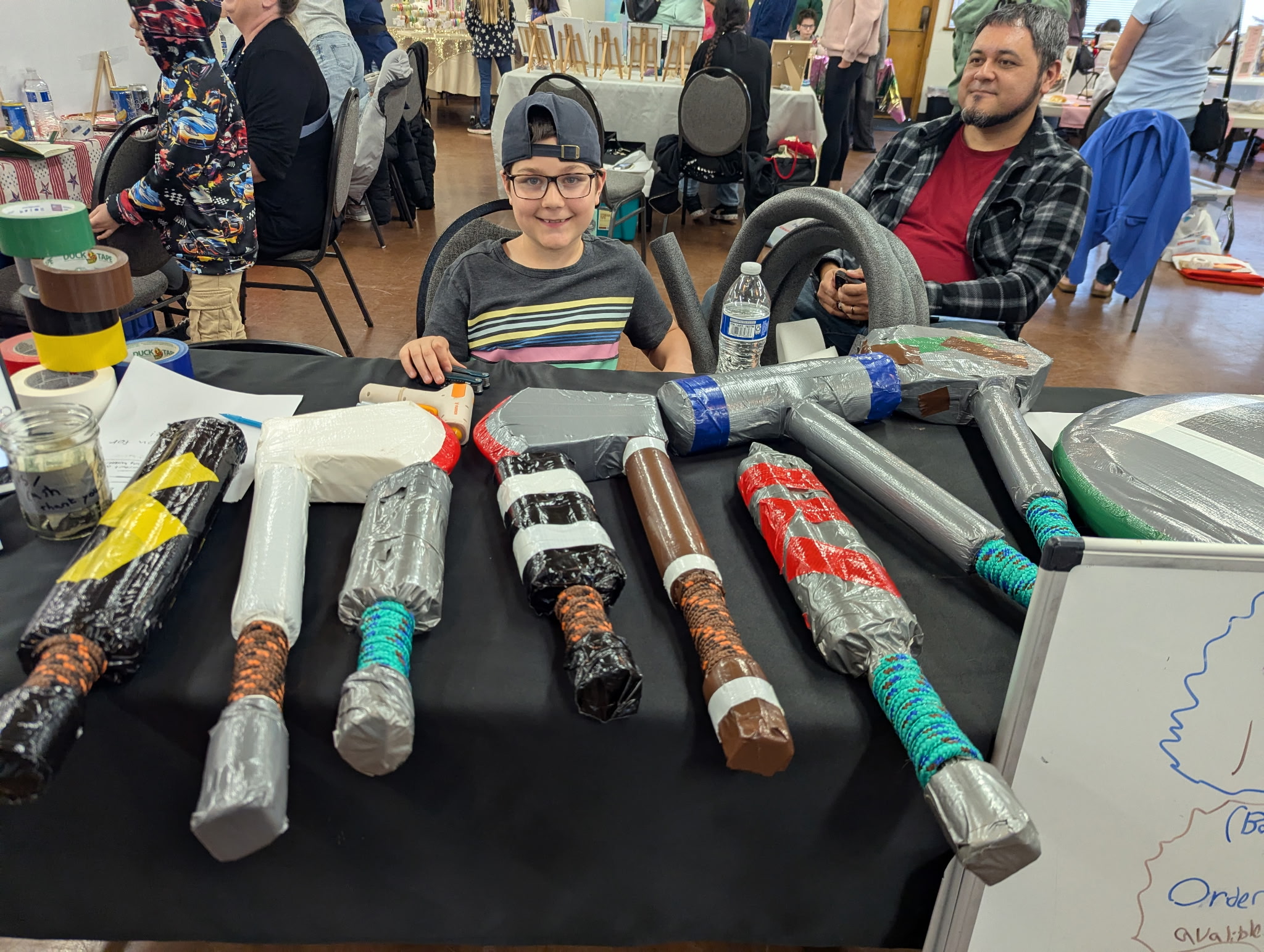 Young entrepreneur selling handmade duct-tape foam weapons at his business fair table