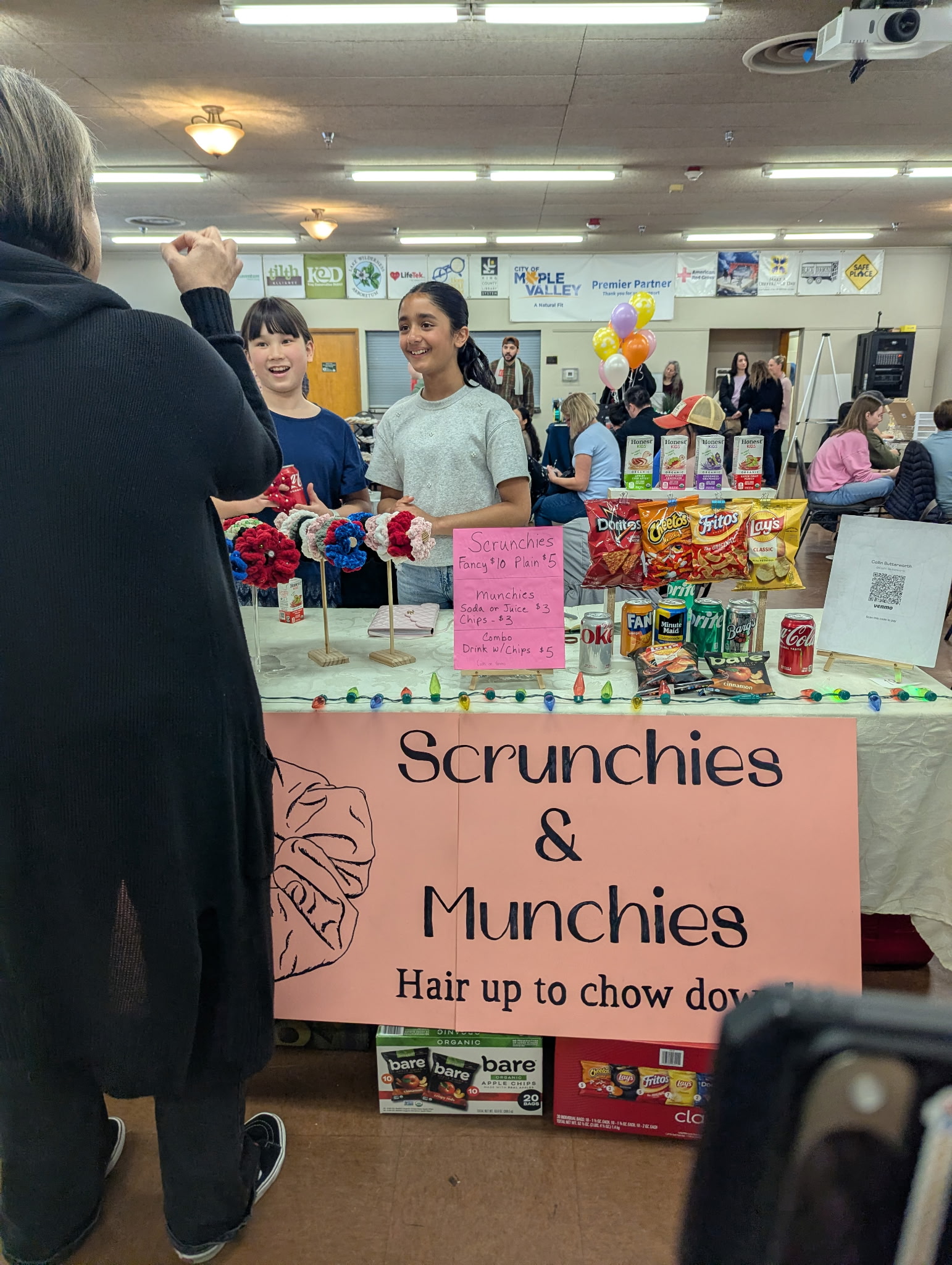 Kid entrepreneurs at their 'Scrunchies & Munchies' booth selling handmade scrunchies, snacks, and drinks